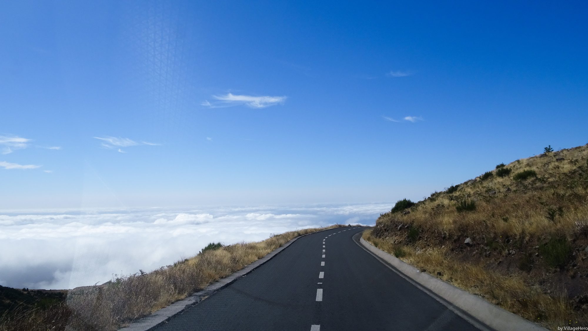 The mountain road near Pico do Arieiro running above a sea of cloud under a clear blue sky