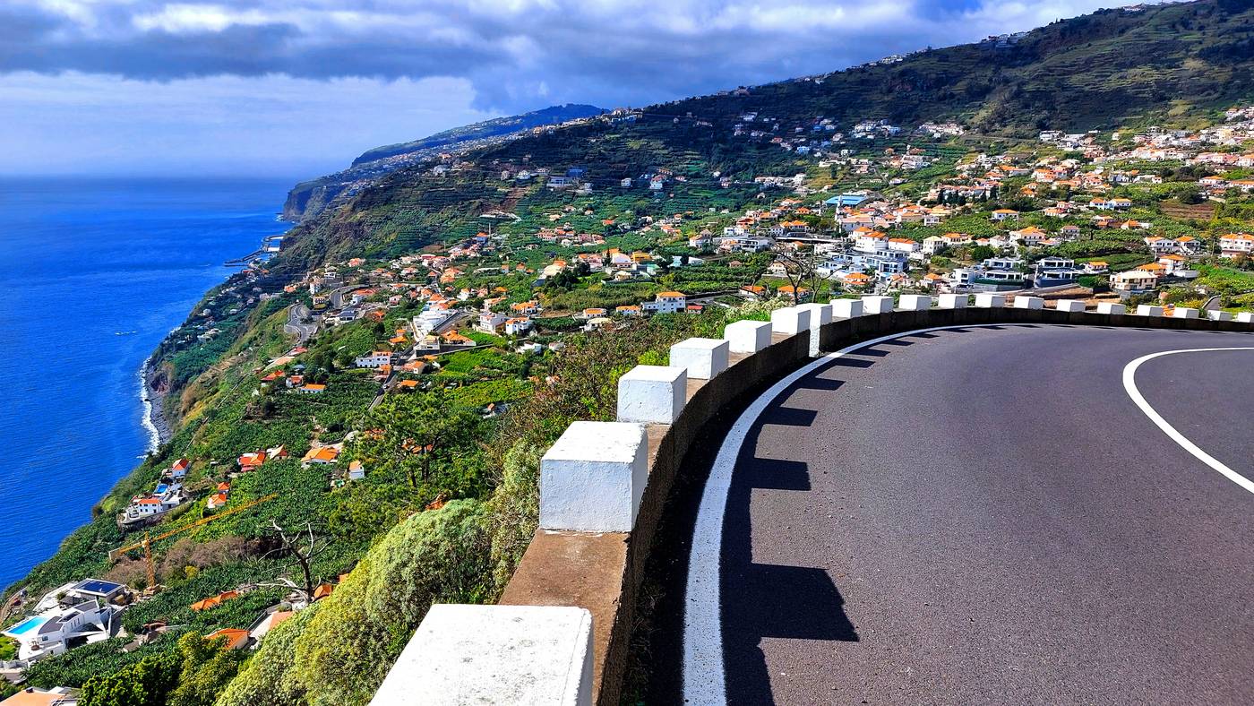 A bend in the coast road with white bollards, high above the banana terraces of Arco da Calheta, the sea below