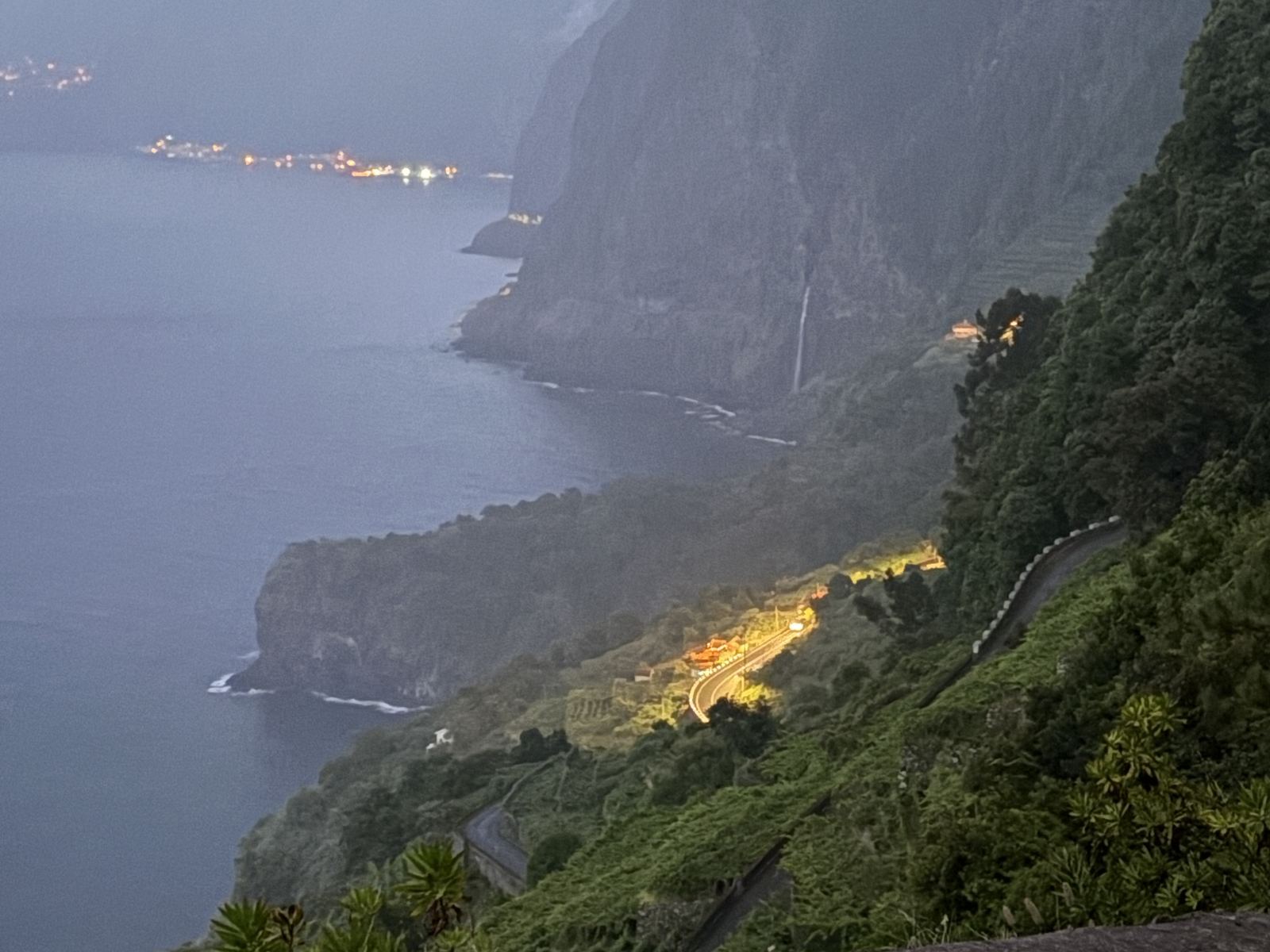 The north coast at dusk from above Seixal, a waterfall on the cliffs and village lights along the shore