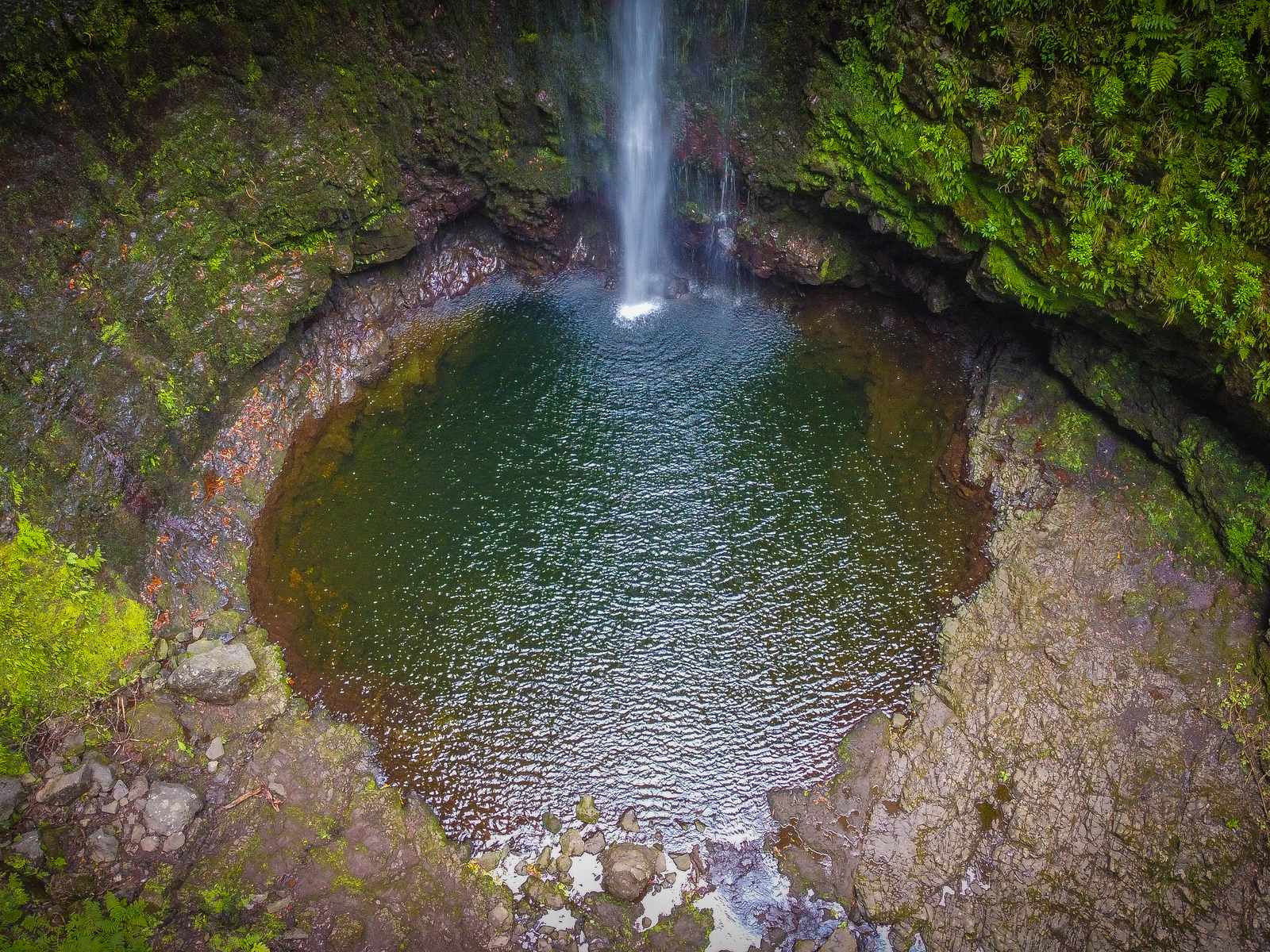 A thin waterfall dropping into the round green pool of Caldeirão Verde, ringed by mossy cliffs