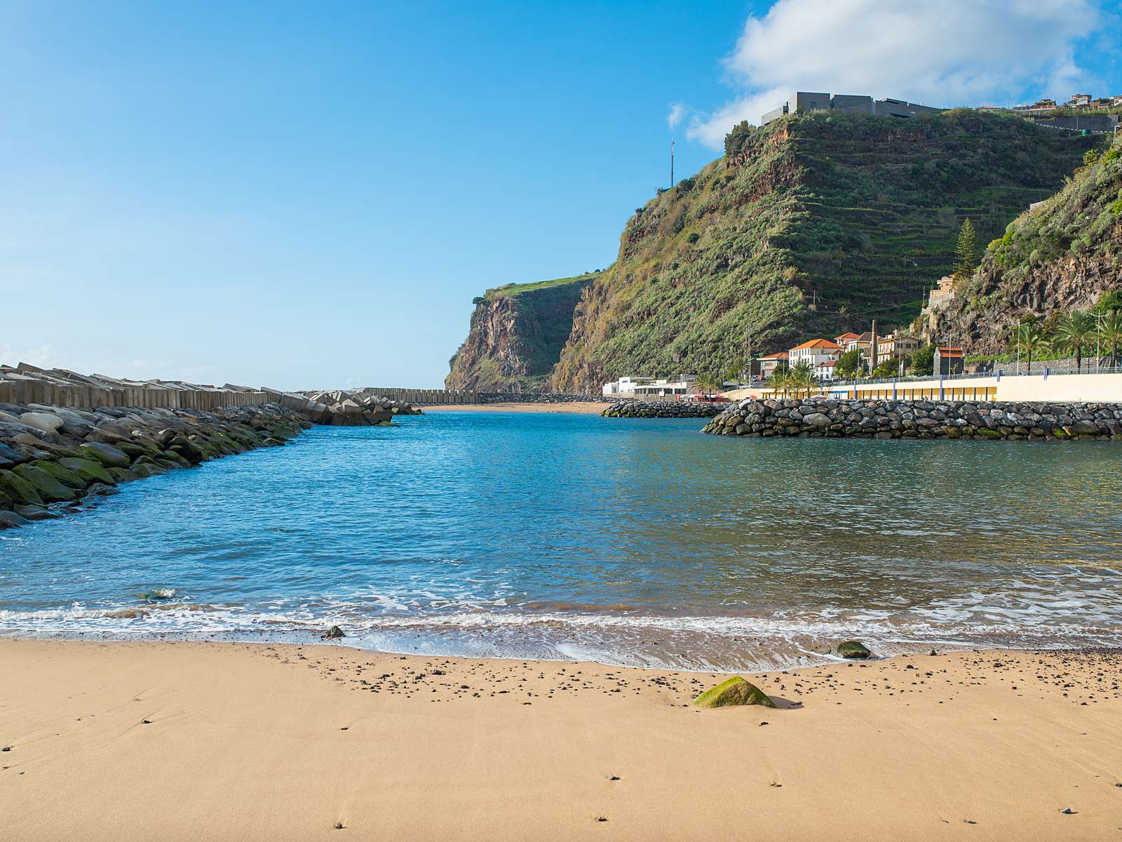 The sand beach at Calheta in its calm lagoon between breakwaters, under a terraced cliff