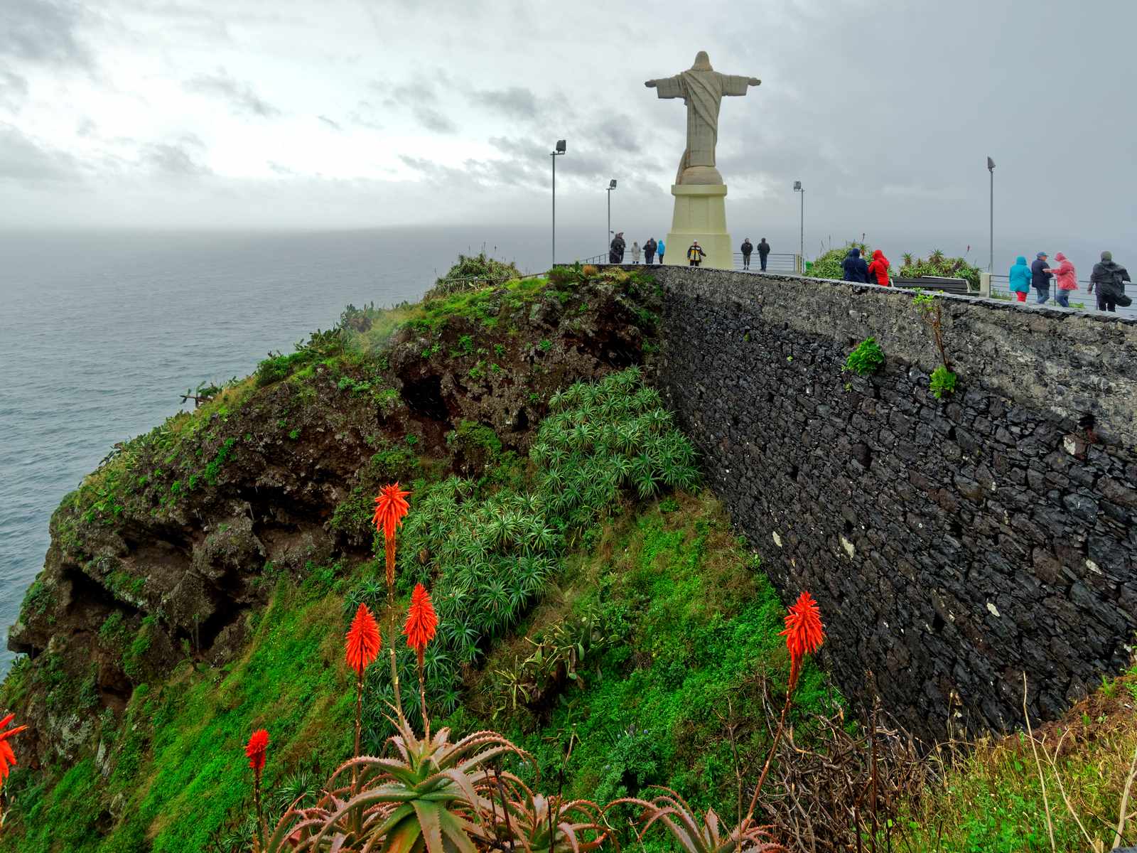 The Cristo Rei statue at the end of the walled headland at Garajau, red aloes in front and the sea beyond