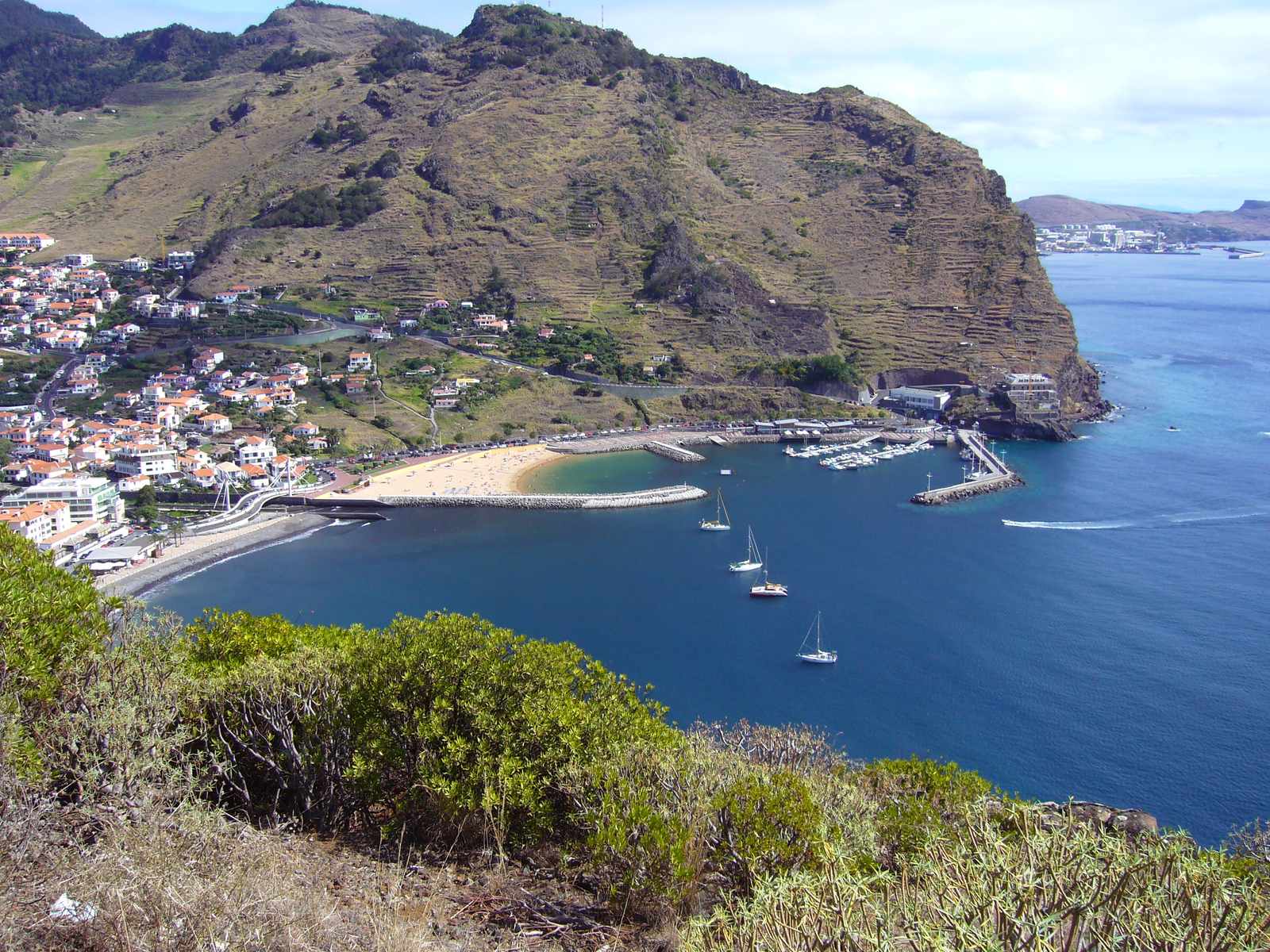 Machico bay from the hillside, the beach, the marina and the town under a terraced headland