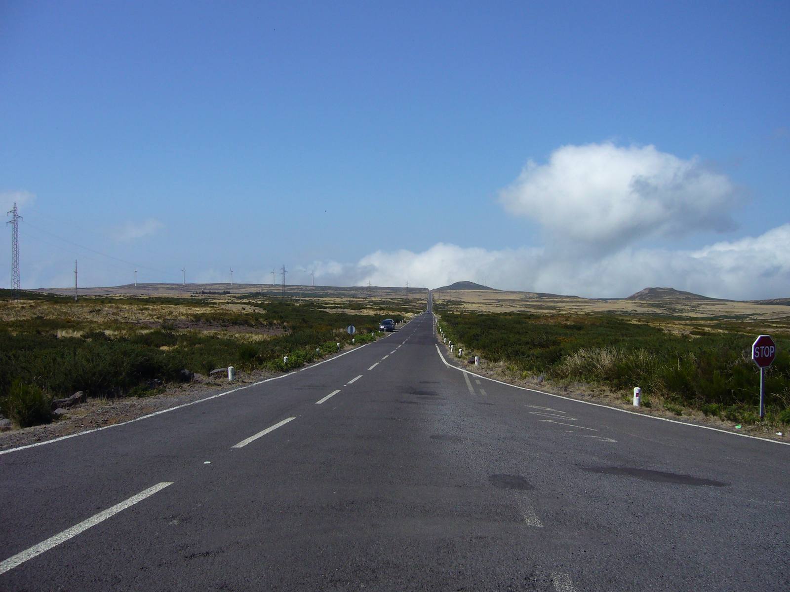 A straight road across the Paul da Serra plateau through low moorland, wind turbines on the horizon
