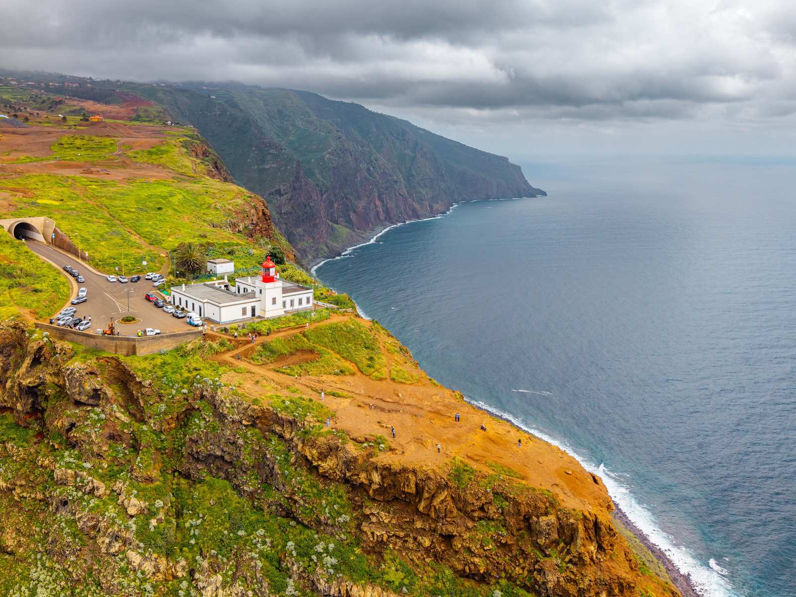 The white Ponta do Pargo lighthouse with its red lantern on the green cliff top above the sea