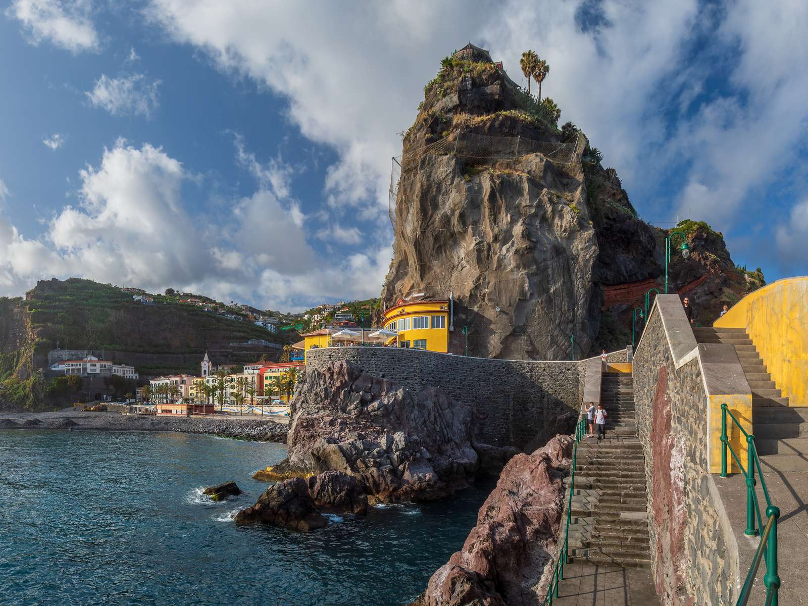The pier rock at Ponta do Sol with its yellow building and stairs, the village and its church across the bay