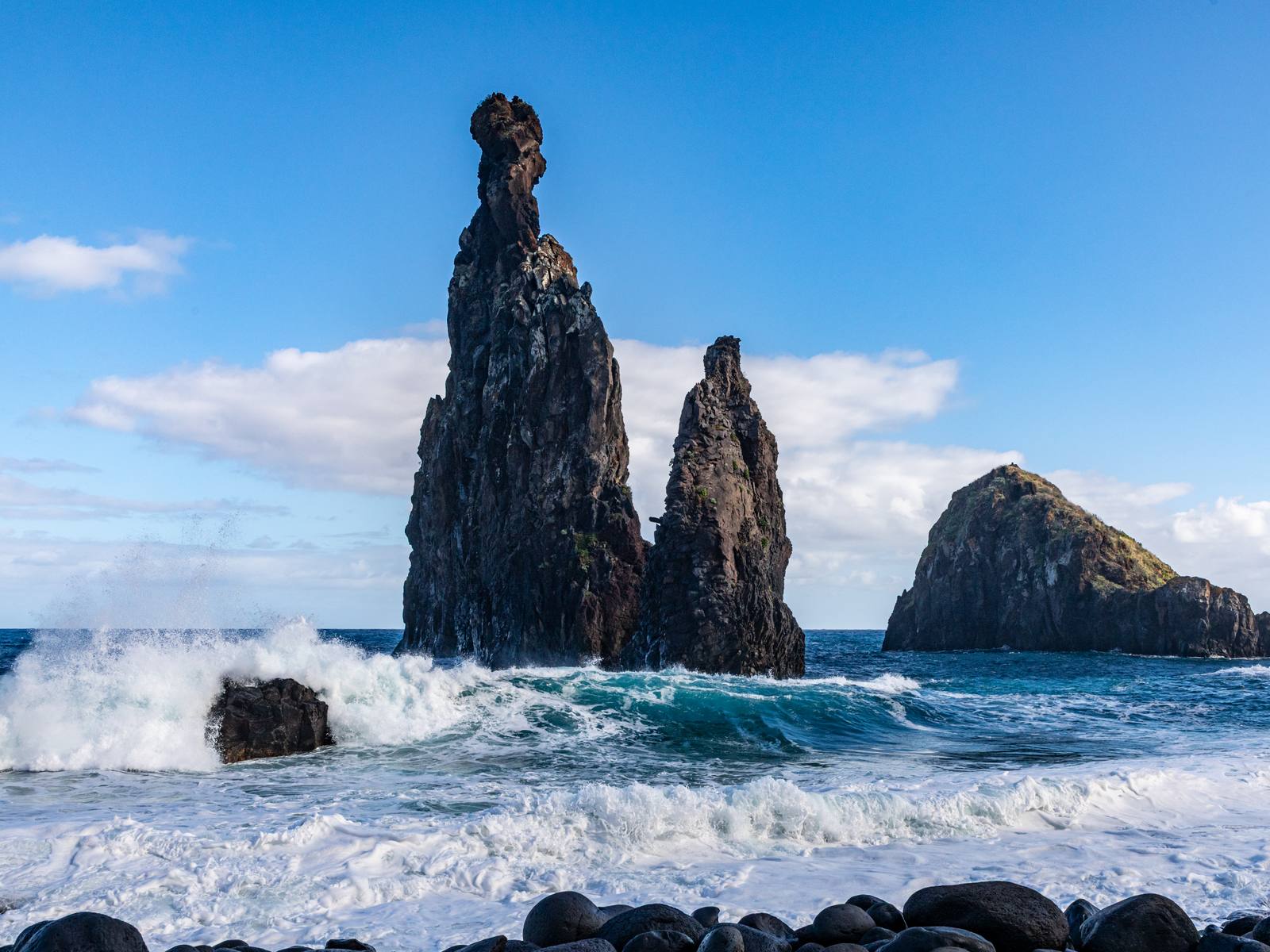 Tall basalt sea stacks rising from heavy surf off the boulder beach at Ribeira da Janela