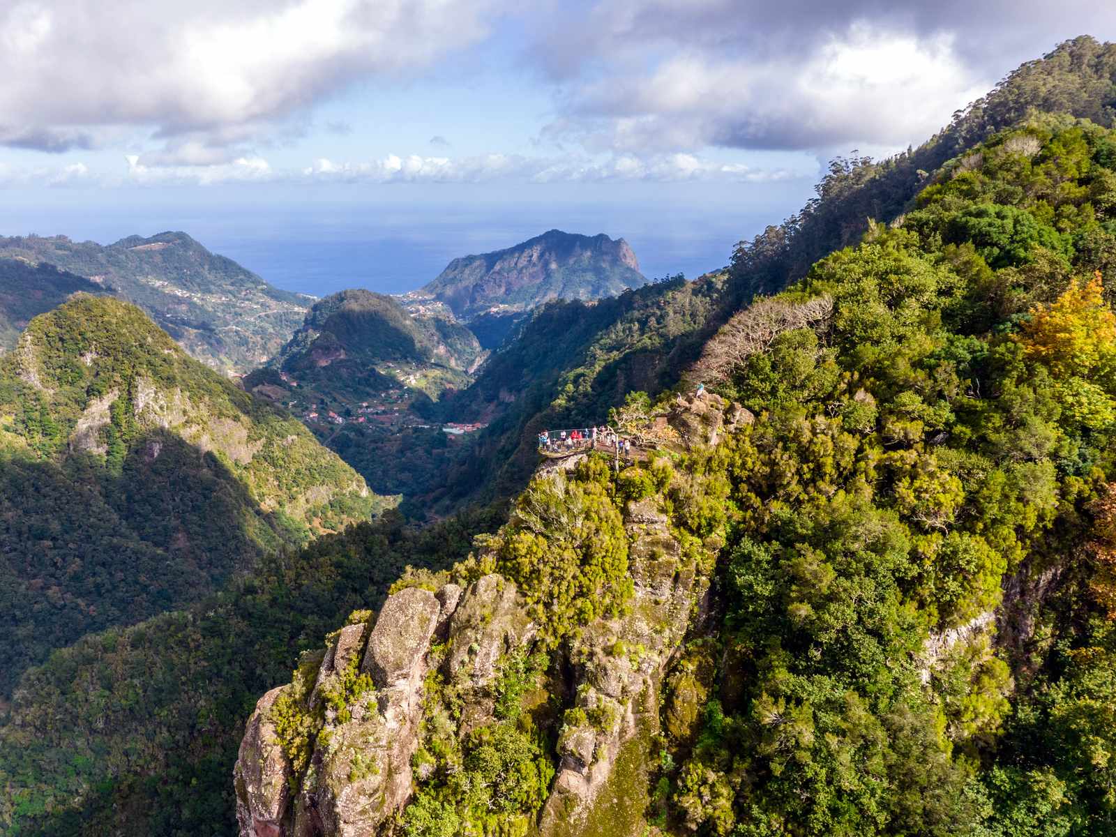 The Balcões viewpoint on a forested ridge, small visitors at its railings, the valley and the north coast beyond