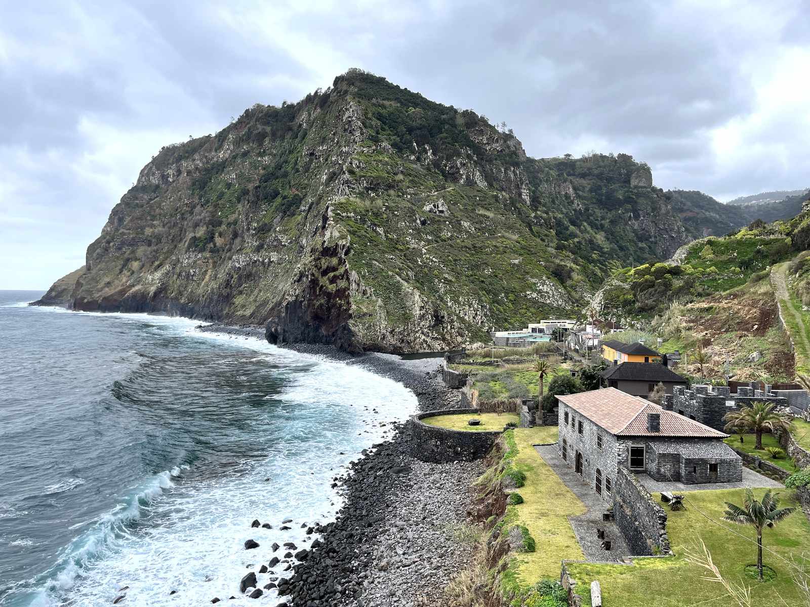 The pebble beach and old stone buildings of the Calhau de São Jorge under a steep green headland