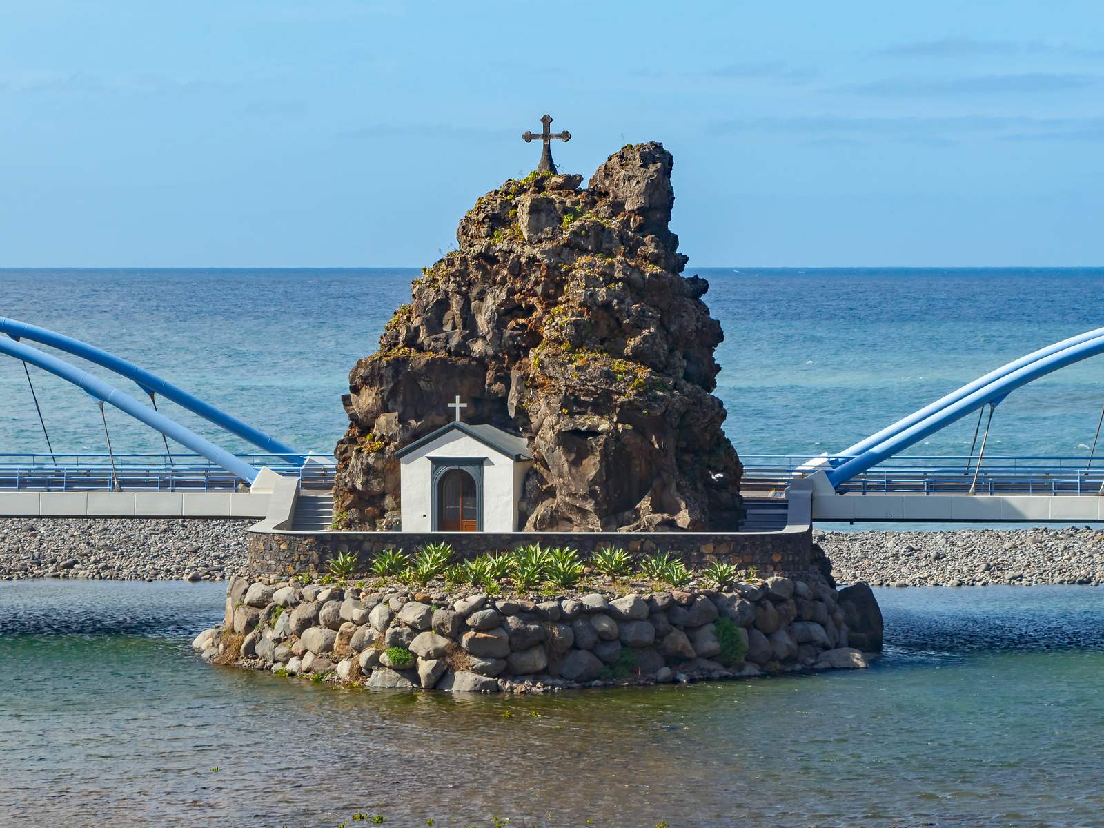 The small white chapel built into a dark rock topped with a cross at the São Vicente river mouth
