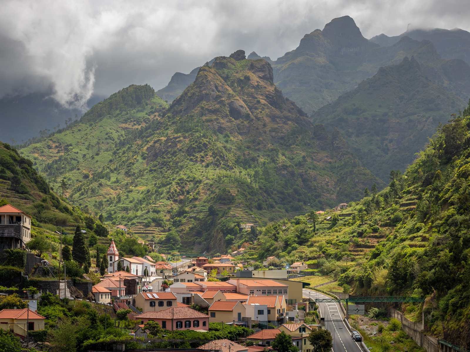 Serra de Água village with its church and orange roofs along the road, under jagged green peaks