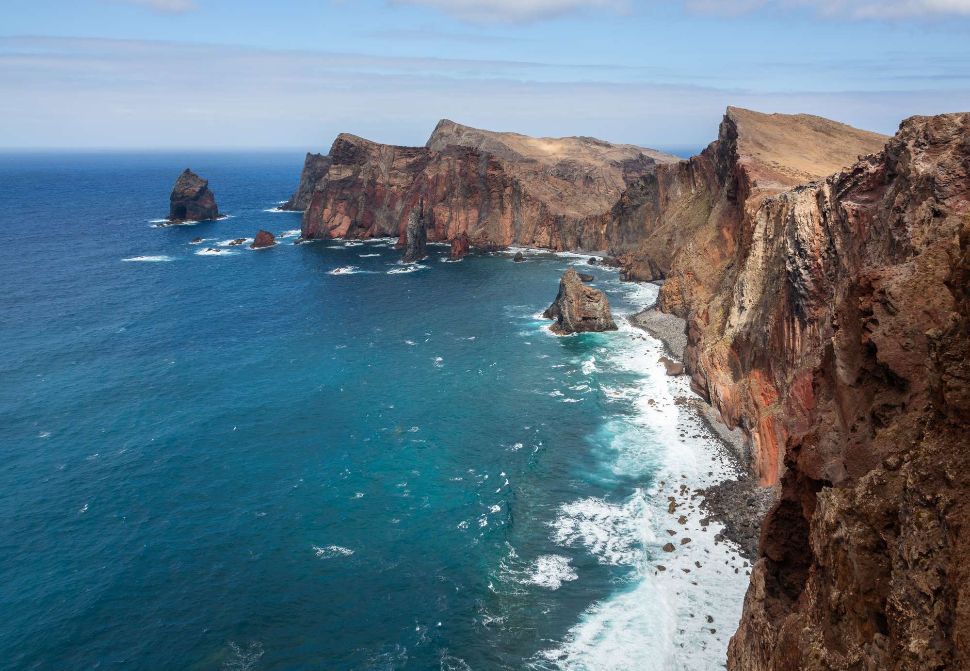 Red cliffs and sea stacks in deep blue water at Ponta de São Lourenço