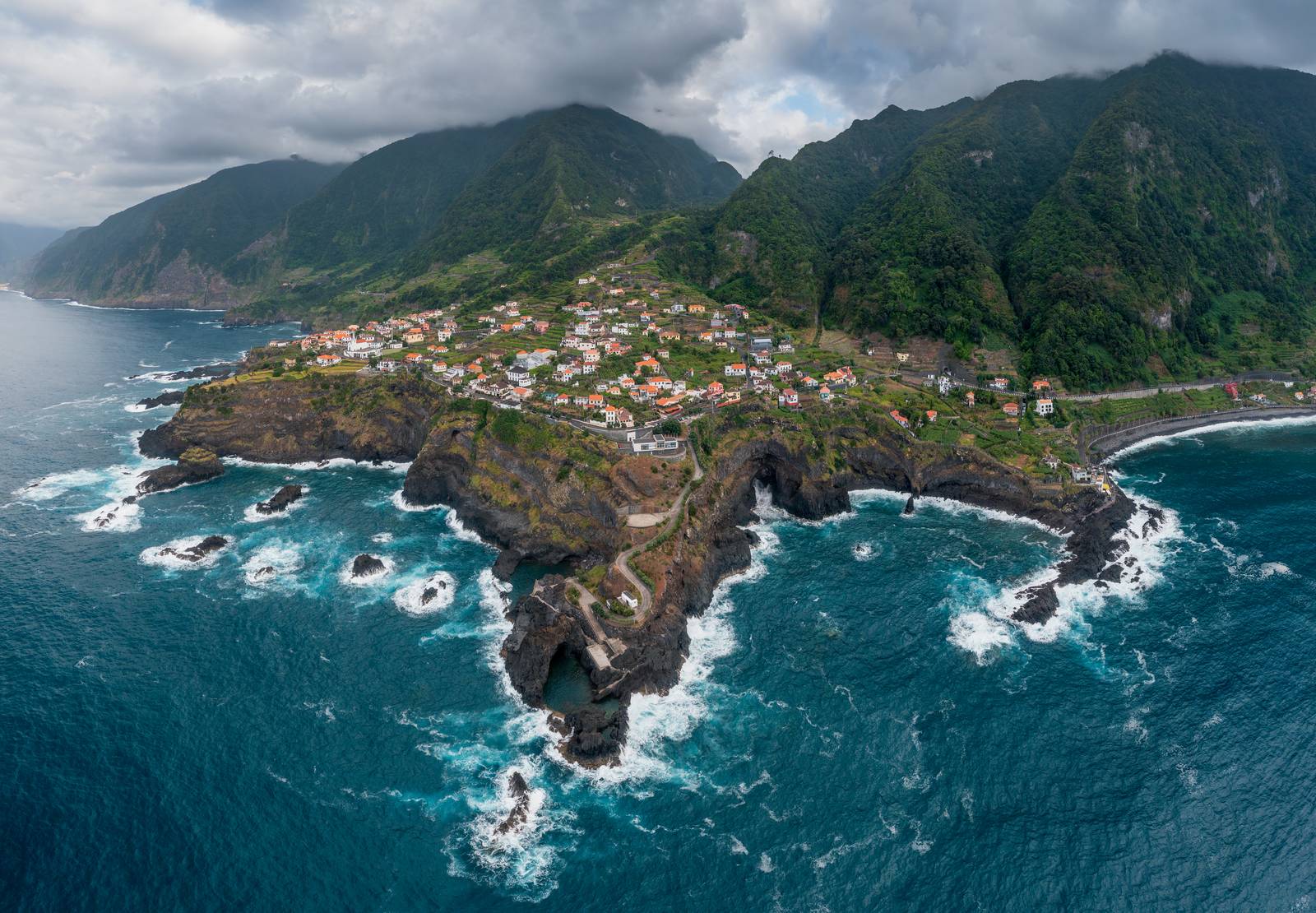 Seixal from the air, the village on its lava headland with surf below and green mountains behind